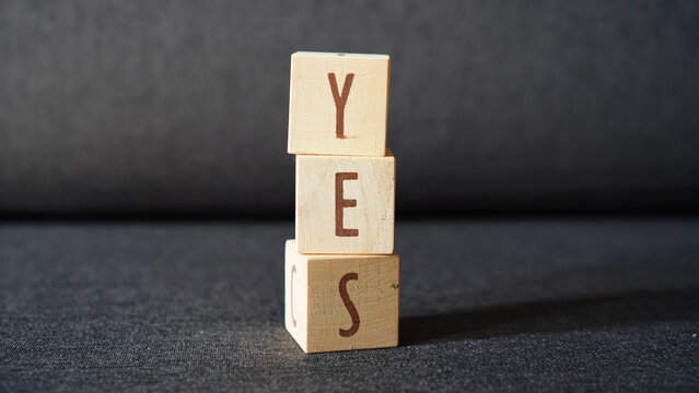 the word "YES" made of arranged wooden cubes, isolated on a dark grey background