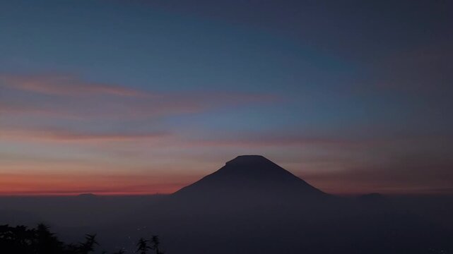 Silhouetted Conical Mountain at Sunset with Misty Landscape