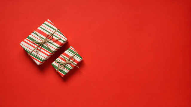 Two christmas gift boxes wrapped in striped paper tied with twine on a red background with copy space
