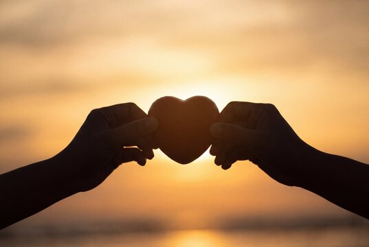 Silhouette of Hands Holding Heart Shape at Sunset for Romance and Charity Concepts