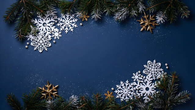 Christmas background with fir branches, white and gold snowflakes on dark blue surface with copy space for text