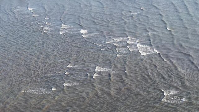 High aerial drone shot of gentle waves and foam patterns over Probolinggo coastal waters.