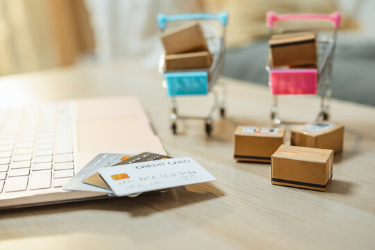 Small delivery boxes reinforce online consumer shopping. Credit card and online shopping relate to online, shopping, and spending; credit card is suggested by the scene. The props are clear.