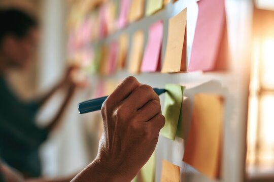 A person writes on sticky notes placed on a wall, likely organizing ideas or planning a project in a creative workspace.