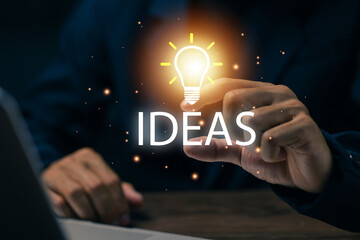 Business professional touching a glowing light bulb and ideas text, representing creative thinking, innovation, inspiration, brainstorming, problem solving, startup planning. © saranyoo