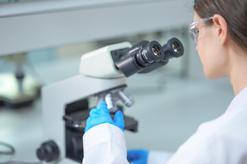 Gloved hand rotating a microscope objective turret selecting a new objective lens in a biosafety lab while screening food samples for Listeria and E. coli contamination © ultramansk