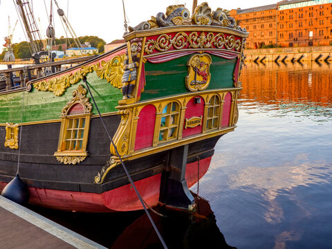 Ornately decorated stern of the historical Libava ship replica with gold carvings, docked in port during golden hour.