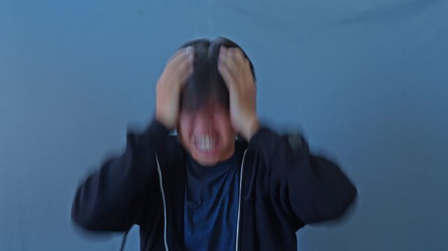 Distressed young man gripping his head in agony during severe mental breakdown portraying bipolar disorder