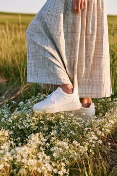Person in white sneakers and plaid skirt standing in a field of