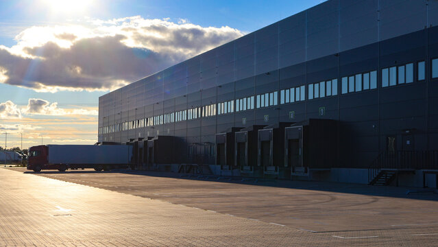Modern distribution warehouse featuring multiple loading docks and a semi trailer truck receiving cargo, representing efficient global supply chain management and industrial transportation at dusk