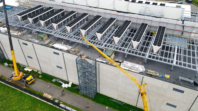 Large data center under construction with rooftop cooling units and cranes installing infrastructure, symbolizing modern computing, cloud scale, energy efficient server farm expansion and innovation