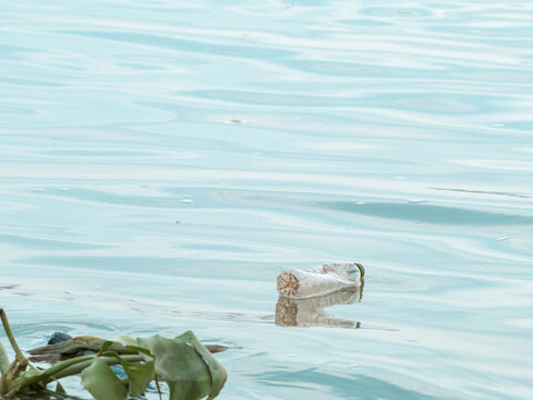 Discarded crumpled plastic bottle with green cap floating on calm pale blue water, river pollution and marine plastic waste environmental problem concept with copy space