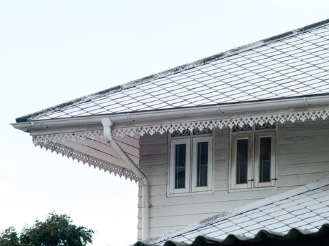 Traditional Thai colonial style house corner with diamond patterned roof, ornate white trim, shuttered windows and gutters, heritage architecture detail