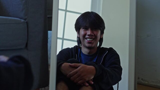 Young man sitting by mirror shifts from laughing to hugging himself in fear depicting bipolar vulnerability