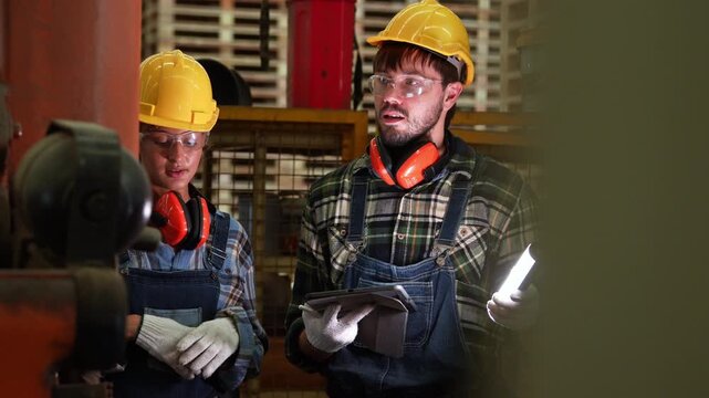 Factory workers collaborate on industrial machinery inspection inside a manufacturing plant, communicating technical updates and focusing on operational safety protocols during production work.