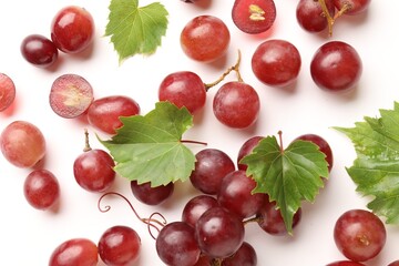 Fototapeta premium Fresh ripe grapes and green leaves on white background, flat lay