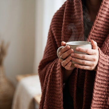 Hands holding steaming mug wrapped in cozy knit blanket, warm drink and hygge comfort concept with copy space for text