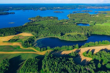 Fototapeta premium Aerial view of vibrant green forests surrounding calm blue lakes and meandering fields