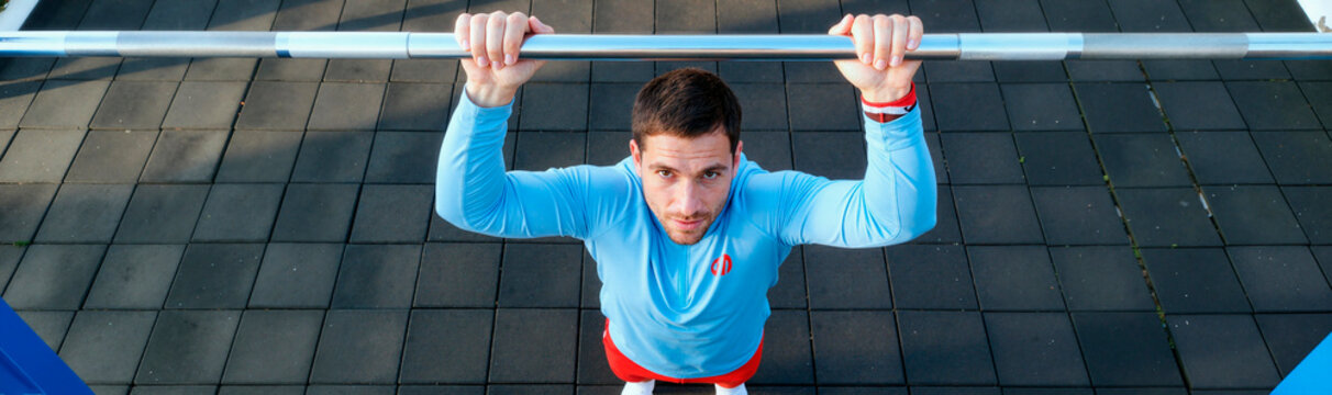 Portrait of Caucasian young adult man gripping pull up bar and exercising outdoors, showing strength and fitness focus. Ideal for gym promotion, wellness campaigns, training content