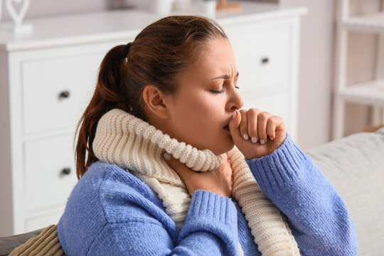 Illness and seasonal flu, woman coughing with sore throat and cold symptoms wearing a warm scarf while sitting at home during winter health crisis