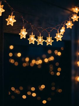 Glowing star shaped string lights hanging against a dark background with beautiful golden bokeh effect