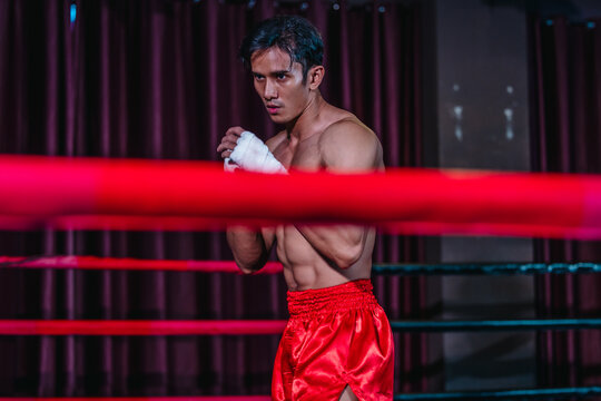 Asian boxer in red shorts shadowboxing behind ring ropes during training before fight