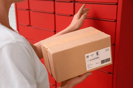 Logistics and parcel delivery, person holding a cardboard box in front of red storage lockers for package collection and e-commerce shipping services