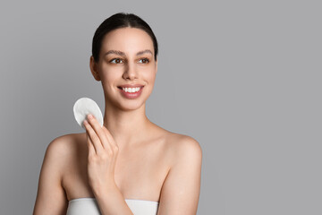 Skincare routine and facial cleansing, young woman using cotton pad for makeup removal and skin care treatment on a neutral gray background © Pixel-Shot