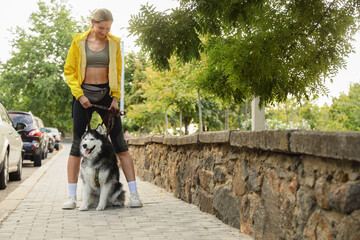 Pet ownership and active lifestyle, young woman walking with her husky dog on a city sidewalk during a sunny day for outdoor recreation and exercise © Pixel-Shot