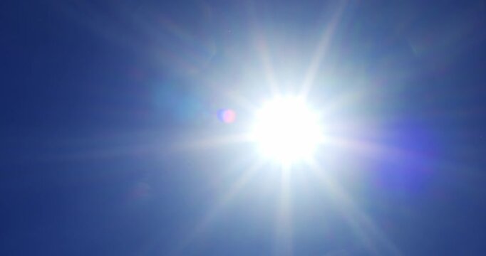 Bright direct sun with lens flare moving across clear blue sky during hot summer day in smooth pan camera movement.