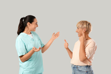 Fototapeta premium Hearing loss and audiology consultation, nurse talking to senior woman with hearing aid device giving thumbs up for successful treatment and care