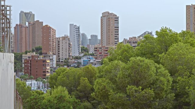A skyline view of Benidorm with high-rise buildings and green trees. The setting is cloudy, reflecting an overcast sky.