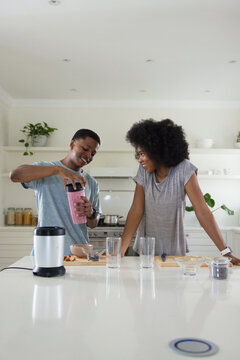 African American couple preparing pink smoothie on island in bright kitchen with personal blender