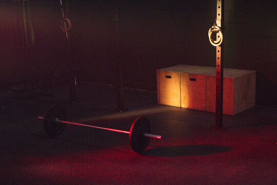 Loaded barbell is resting on textured rubber floor in dim gym, casting elongated shadow