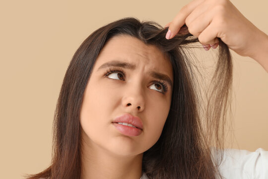Hair loss and thinning hair concerns, young woman checking split ends and damaged hair with worried expression on a neutral studio background