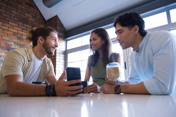 Diverse friends leaning at glossy white table in modern lounge, holding smartphone and glass mug © WavebreakMediaMicro