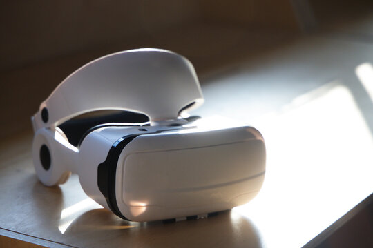 White VR headset visor facing viewer, resting on light wood tabletop, showing black trim and strap