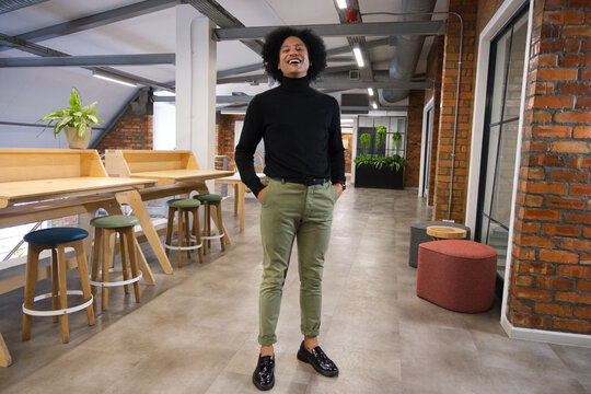 Man standing and laughing in coworking corridor by wooden workbench with plants