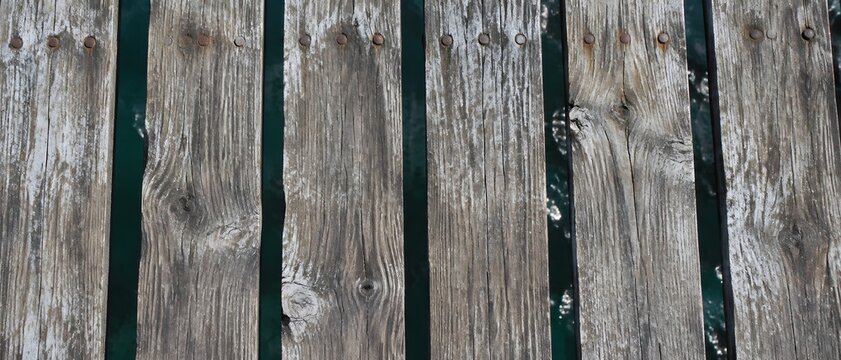 Weathered timber pier deck seen from directly above with parallel boards and rusted nail heads