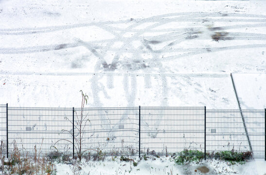 First winter snow covering parking lot ground with tire tracks and footprints