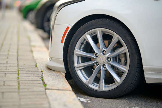 Minsk, Belarus. Jun 6, 2025. Cadillac car wheel, tight parking position of silver rim and black tire against brick pavement, hazard to disc and rubber tire. Careless parking. front bumper touches curb