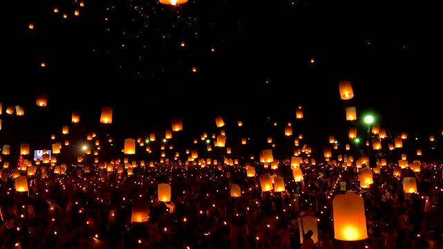 People gather at night to watch glowing lanterns float into the sky during a lantern release festival,
