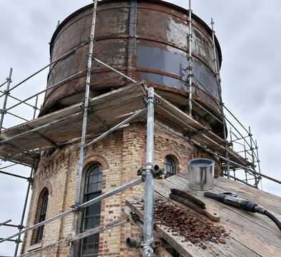 Brick Victorian water tower with scaffold and rust converter on tank