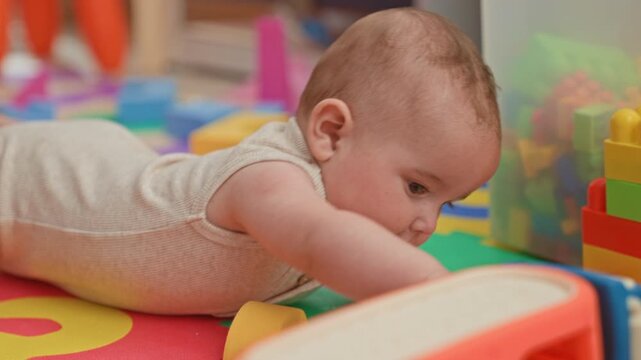 Baby on tummy reaching for a colorful toy on a foam playmat, hand gripping a block in building; curiosity innocence.