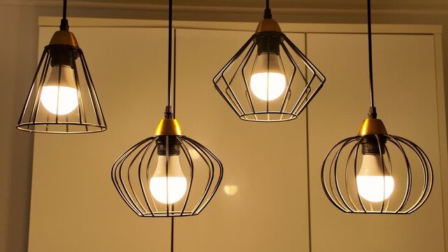 Four designer pendant lamps with black metal cage shades and warm led bulbs illuminating a contemporary interior space, concept of home decor