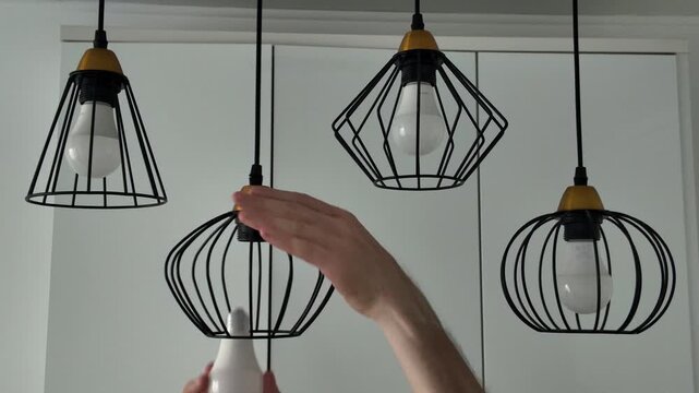 A man installs a new energy-saving LED light bulb into a modern ceiling light fixture, restoring the lighting