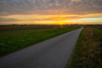 Fototapeta premium A rural, asphalt road in Germany at sunset
