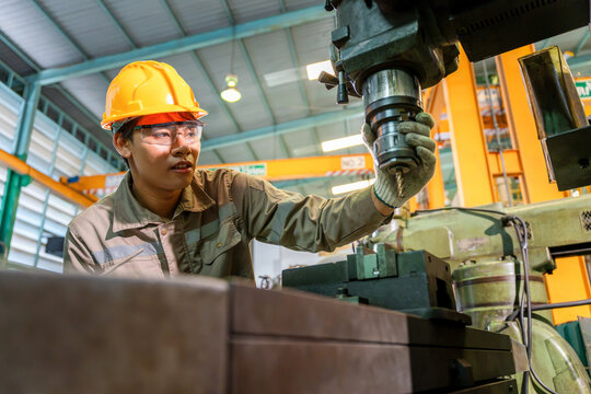 Asian factory worker operating heavy machinery and drilling equipment in manufacturing plant, industrial technician controlling milling machine tool in production factory production line