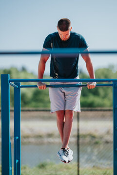 A young man performs a dip hold on outdoor parallel bars during a calisthenics workout. He balances with straight legs on blue fitness bars in an outdoor training area.