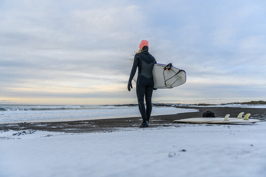Female surfer with surfboard on a snowy beach